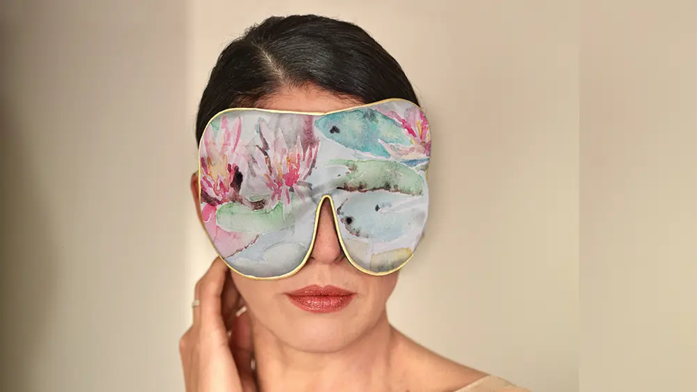 Water Lilies patterned silk sleep mask with honey‑coloured piping worn by a person against a neutral background