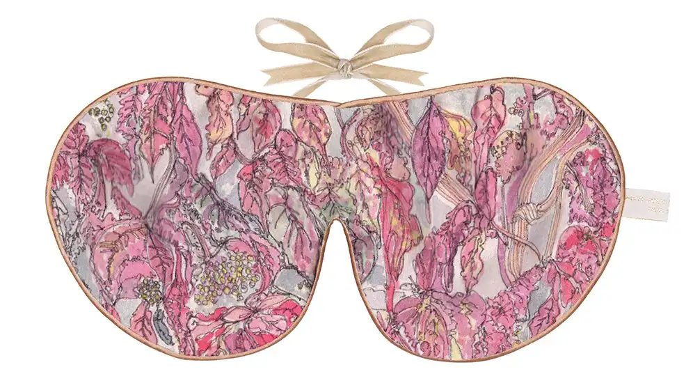 Silk sleep mask with a detailed pattern of pink, mauve, and red leaves layered over a subtle textured background.