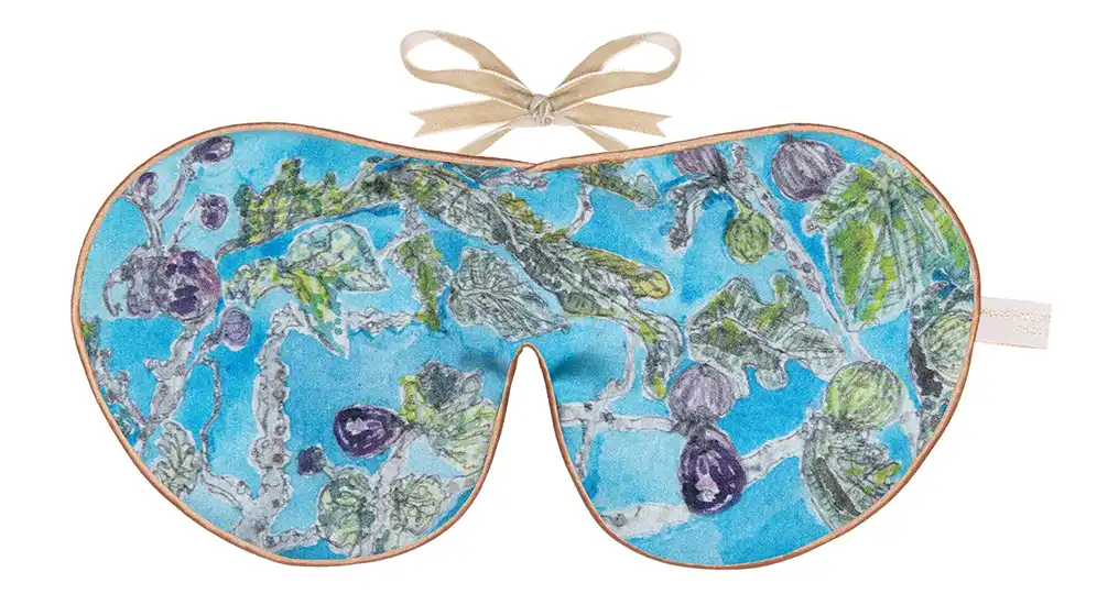 Silk sleep mask with a blue background featuring hand‑drawn fig leaves and ripe figs in shades of green and purple.