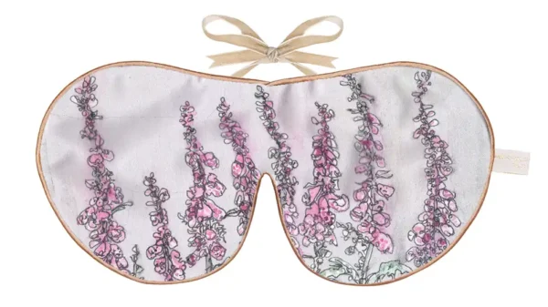 Silk sleep mask featuring a botanical illustration of tall pink foxglove flowers on a light background, finished with warm piping and a beige ribbon tie.