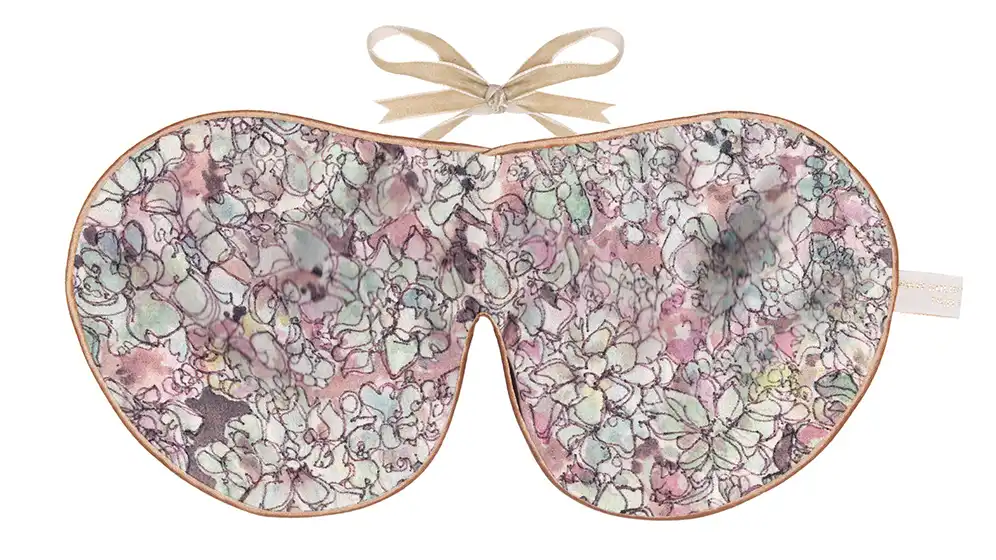 A patterned silk sleep mask with a pastel floral design and a beige ribbon tie.