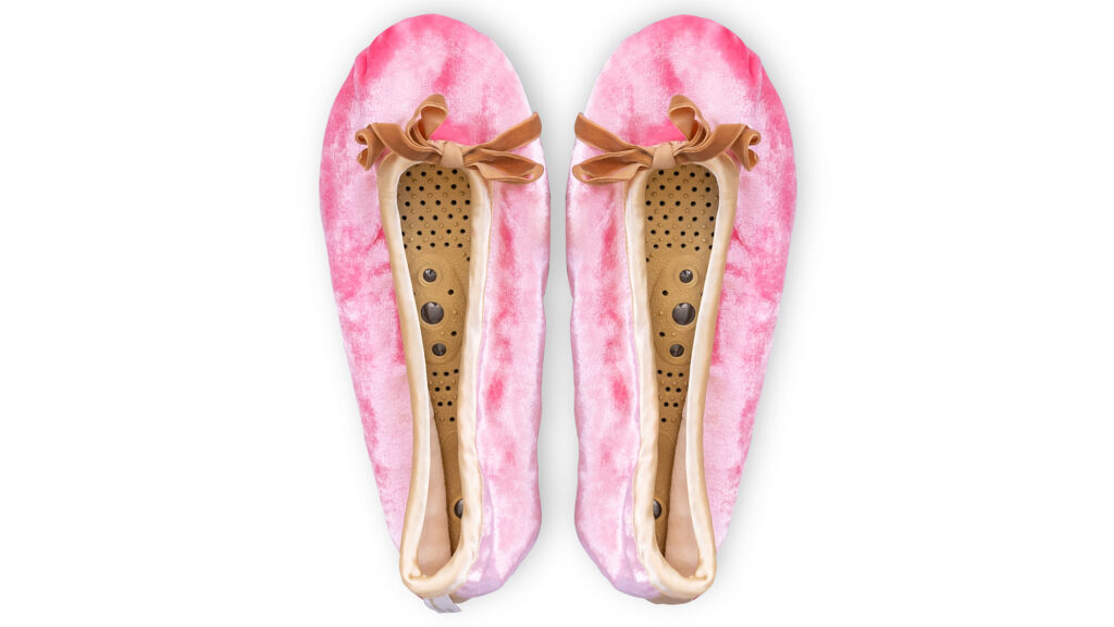 A flat image of a pair of Holistic Silk ballerina style Massaging Slippers in a Rose Silk Velvet colour with a honey colour velvet bow tie at the top edge of the toe area. The slippers are side by side with the toes at the top of the image. The magentic insoles inside the slippers are visable.