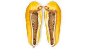 A flat image of a pair of Holistic Silk ballerina style Massaging Slippers in a Sundrop Yellow Silk Velvet colour with a honey colour velvet bow tie at the top edge of the toe area. The slippers are side by side with the toes at the top of the image. The magentic insoles inside the slippers are visable.
