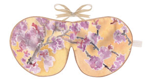 Flat image of the Holistic Silk Excluisve Silk Sleep Mask with a watercolour effect hand drawn Cherry Blossom branch on a yellow background with Honey colour piping and a Honey colour velvet bow above it on a clear white background.