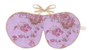 Flat image of the Holistic Silk Limited Edition Brocade Sleep Mask in a Lilac Bloom design featuring lilac blooms in varying shades of pink & purple on a lilac colour background with Honey colour piping and a Honey colour velvet bow above it on a clear white background.