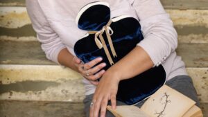 A middle torso short of a gir holding a Holiostic Silk Silk Velvet Hot Water Bottle in a navy colour against ehr body.