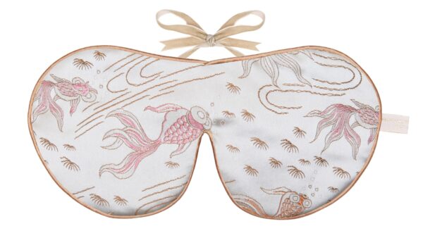 A silver silk sleep mask embroidered with flowing goldfish and water motifs in peach, rose‑gold, and gold threads, finished with gold edging and beige ribbon ties