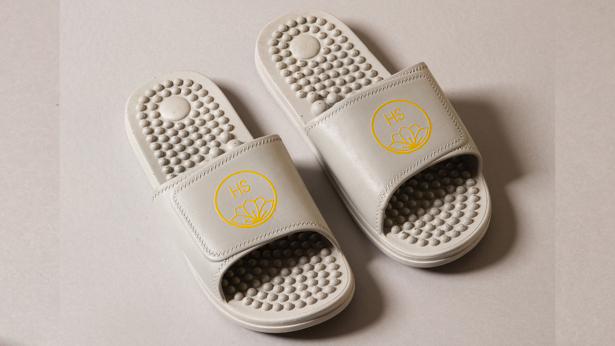 Pair of silver PVC massaging sliders with raised footbed texture on a light background