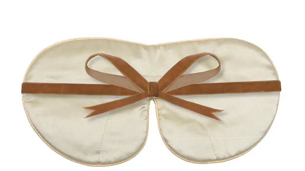 Reverse view of a cream pure silk sleep mask with honey‑coloured piping and matching silk ribbon strap, laid flat against a white background.