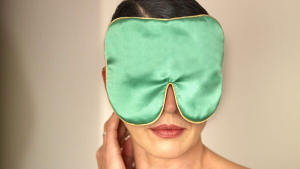 Person wearing an extra large jade silk eye mask with gold piping, shown from the front against a soft neutral background.