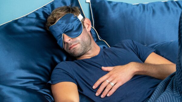 Person reclining on a bed dressed in blue sleepwear, surrounded by large navy satin pillows with light piping.