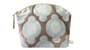 A flat image of the Holistic Silk Lavender Make up Bag in a British Jade Brocade on a white background. The design shows an abstract 2 toned pale jade rounded flower in a linear design on a broze gold background. The wash bag is stood up and is wider at the top than the bottom, it has a curved zipped top which has a honey colour piping outlining it and the zip pull hanging to the top left of the bag.