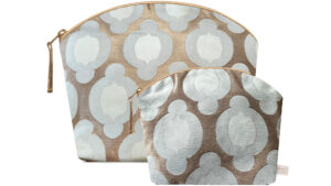 A flat image on a white background showing the Holistic Silk Lavender Wash Bag at the rear with the Holistic silk Lavender Make up bag in front to demonstrate the size difference. Both bags are in a British Jade Brocade design which has an abstract 2 toned pale jade rounded flower in a linear design on a bronze gold background. Both bags are stood up and each are wider at the top than the bottom, have curved zipped tops which have honey colour piping outlining them and the zip pulls are hanging to the top left of each bag.