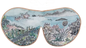 Silk sleep mask with an illustrated coastal landscape featuring succulents, rocks, and distant mountains in soft greens and blues.