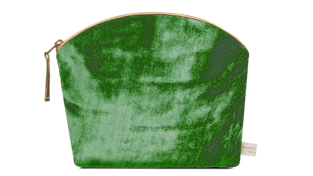An emerald green silk velvet makeup bag with a curved top, gold zipper, and soft shimmering texture.