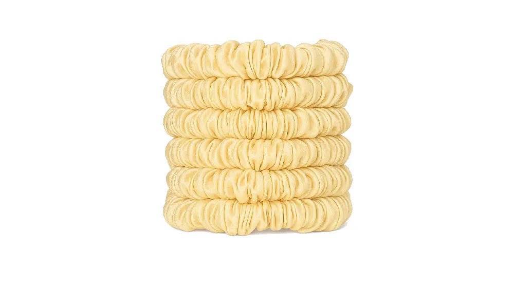 A stack of skinny silk scrunchies in a Cream shade, neatly arranged to show their smooth gathered texture