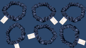 Six navy blue satin silk scrunchies displayed on a dark blue background, each with a white fabric tag.