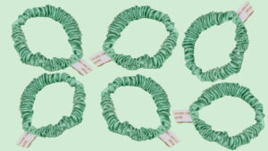 Six jade green satin scrunchies set on a pale mint-green background, each with a white tag.
