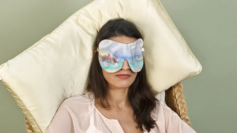 Person reclining on a chair wearing Felos Bay exclusive silk sleep mask with honey trim