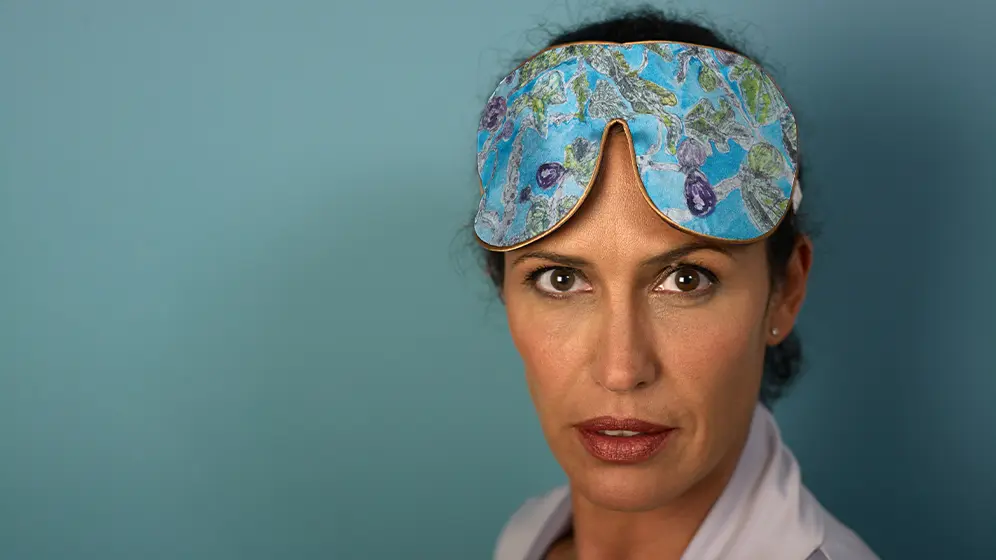 Close‑up of Fig Tree exclusive silk sleep mask with honey‑coloured trim worn against a teal background