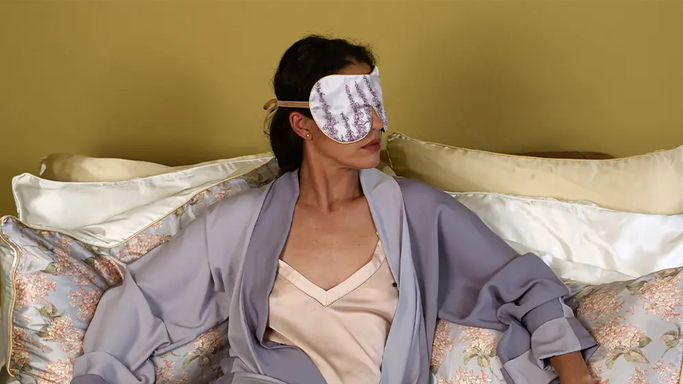 Person resting on cushions wearing Foxgloves exclusive silk sleep mask with honey trim
