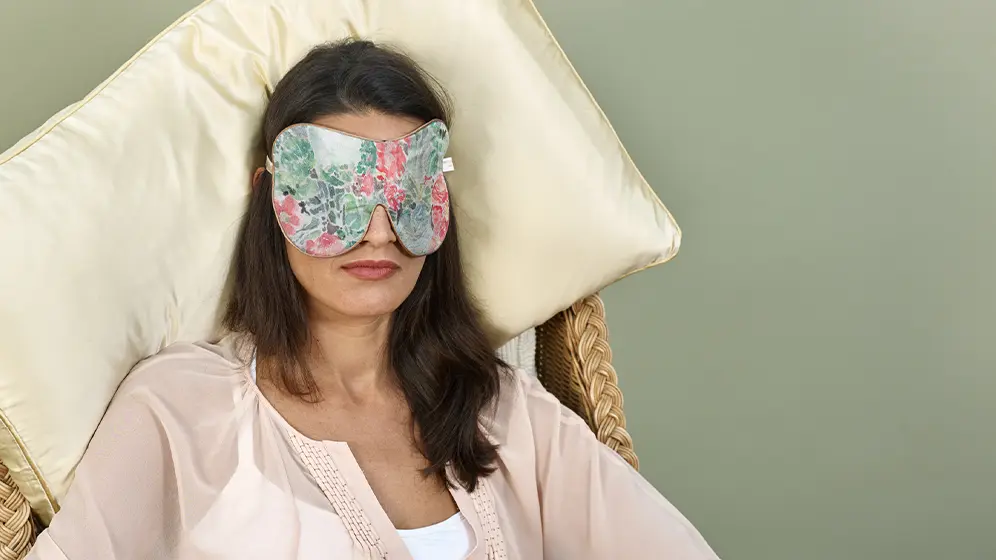 Person resting on chair wearing Nasturtium exclusive silk sleep mask with honey‑coloured trim