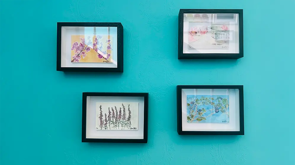 Four framed botanical art prints by Joanna Weakley, arranged on a jade wall, featuring delicate floral illustrations in black frames with white mounts.