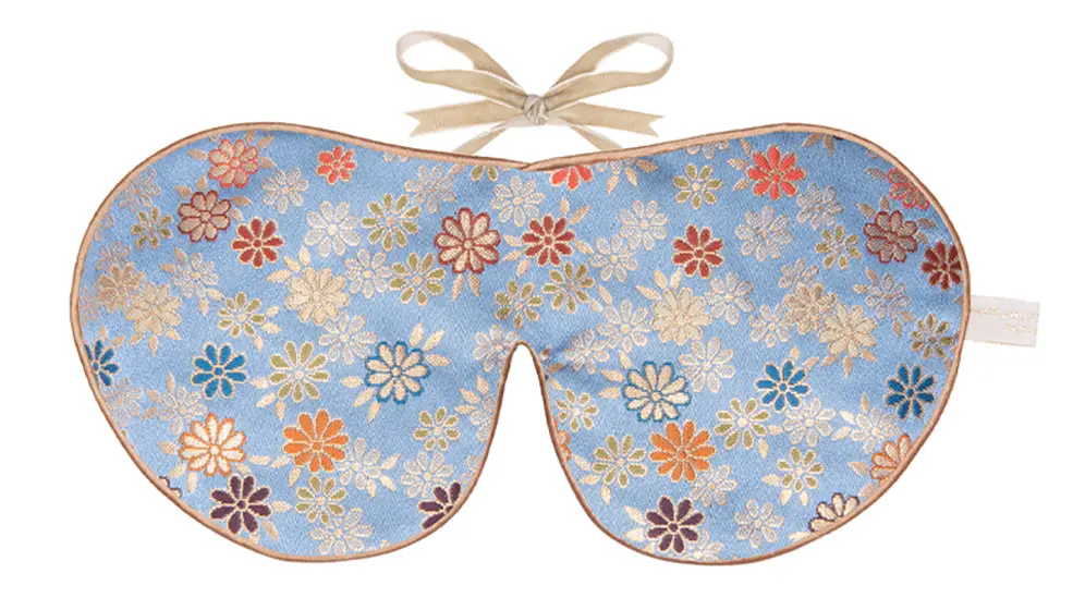 Lavender blue silk sleep mask with scattered floral pattern and honey coloured trim with ribbon fastening