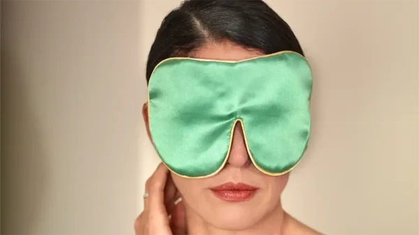 Jade pure silk sleep mask with honey‑coloured piping shown from the front while worn against a soft neutral background.