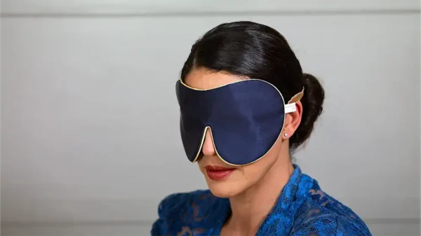 Navy pure silk one strap sleep mask with honey coloured piping worn on a model, shown in side view against a neutral background.