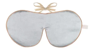 A silver silk sleep mask is displayed flat against a white background. The mask is made from silk and has a smooth surface with a soft reflective sheen. The shape is wide and contoured to fit over the eyes, with a curved centre section for the bridge of the nose.