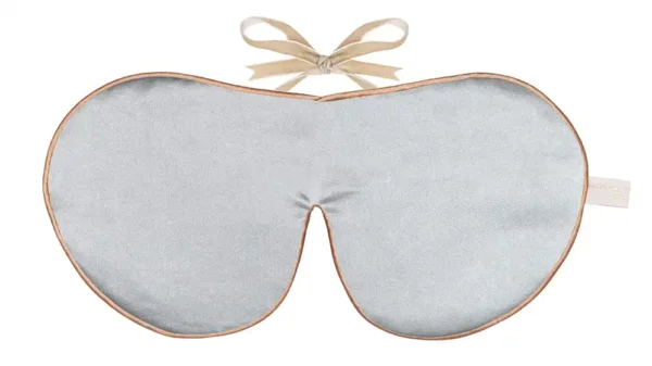 A silver silk sleep mask is displayed flat against a white background. The mask is made from silk and has a smooth surface with a soft reflective sheen. The shape is wide and contoured to fit over the eyes, with a curved centre section for the bridge of the nose.