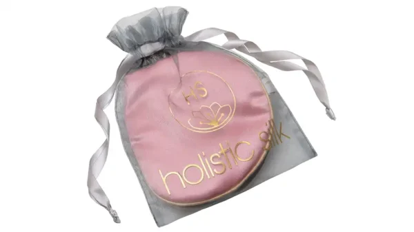 Pure silk rose pink eye mask with honey‑coloured trim, embroidered Holistic Silk logo, presented inside a sheer silver organza drawstring bag.